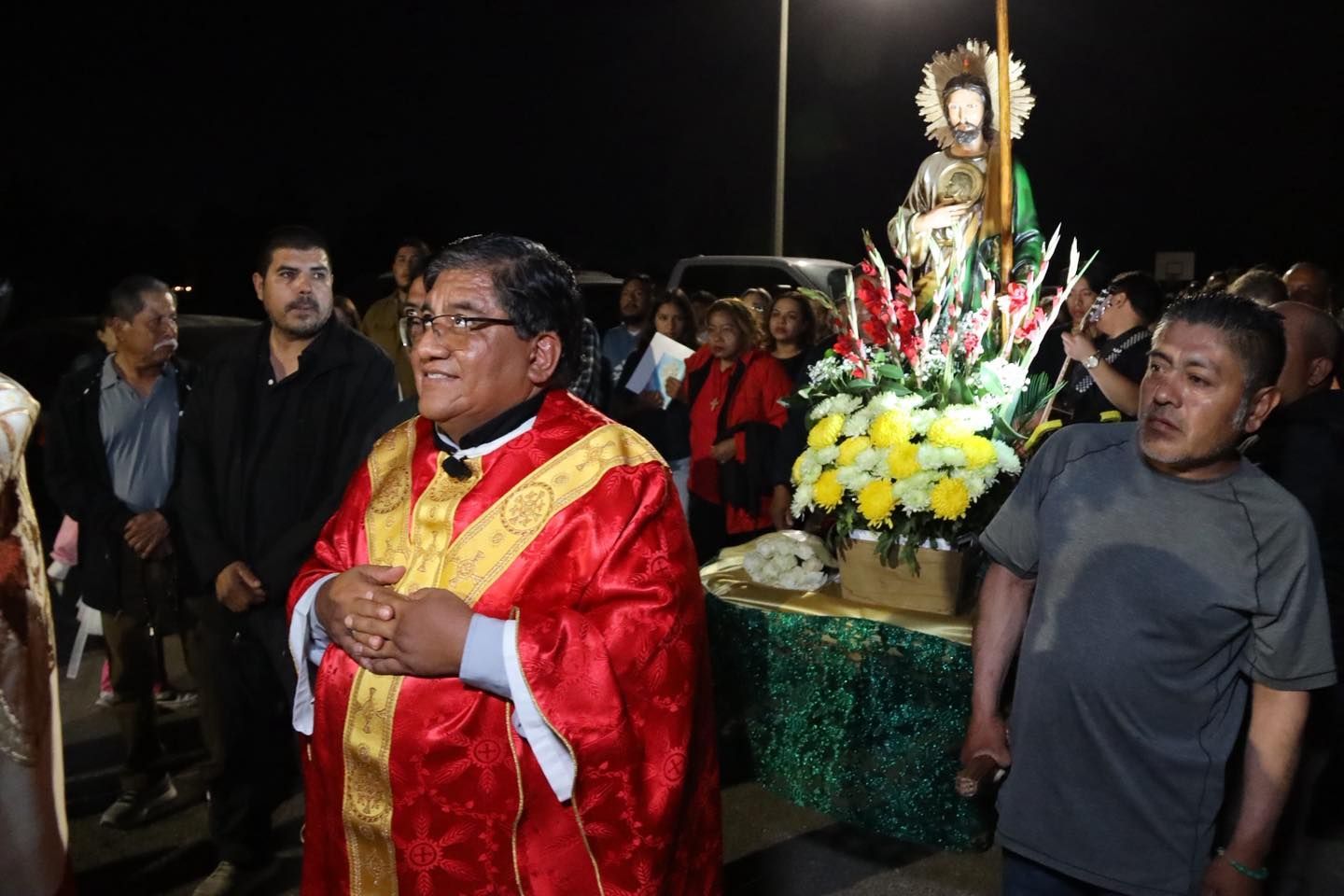 Night procession with a red-robed man carrying a lit statue on a decorated platform