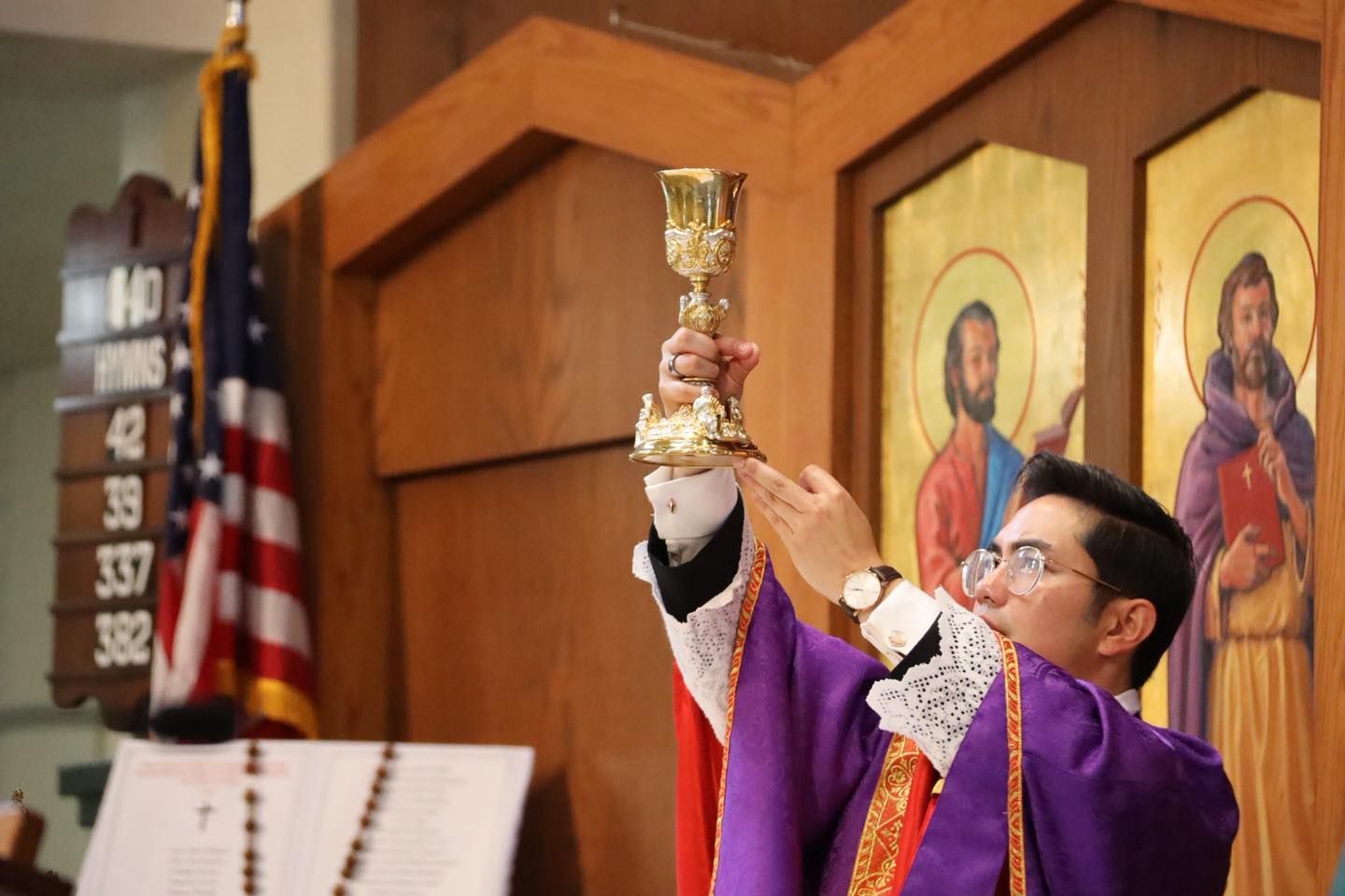 Priest in purple vestments raising a chalice during a church service before religious icons