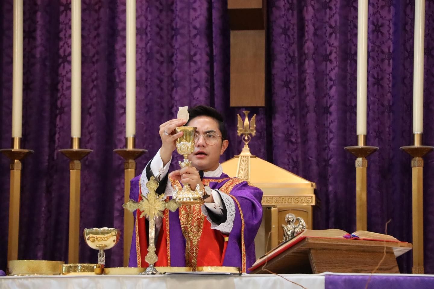 Priest elevating the Eucharist at an altar with purple drapes and gold vessels