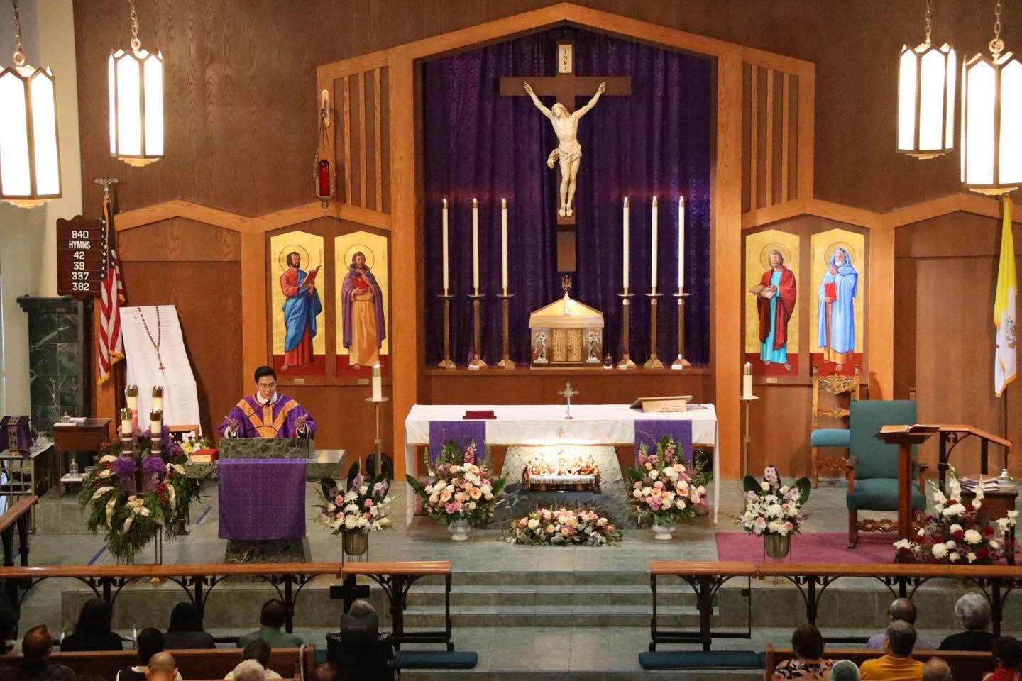 Church altar with crucifix, purple drapes, and floral arrangements inside a wooden sanctuary
