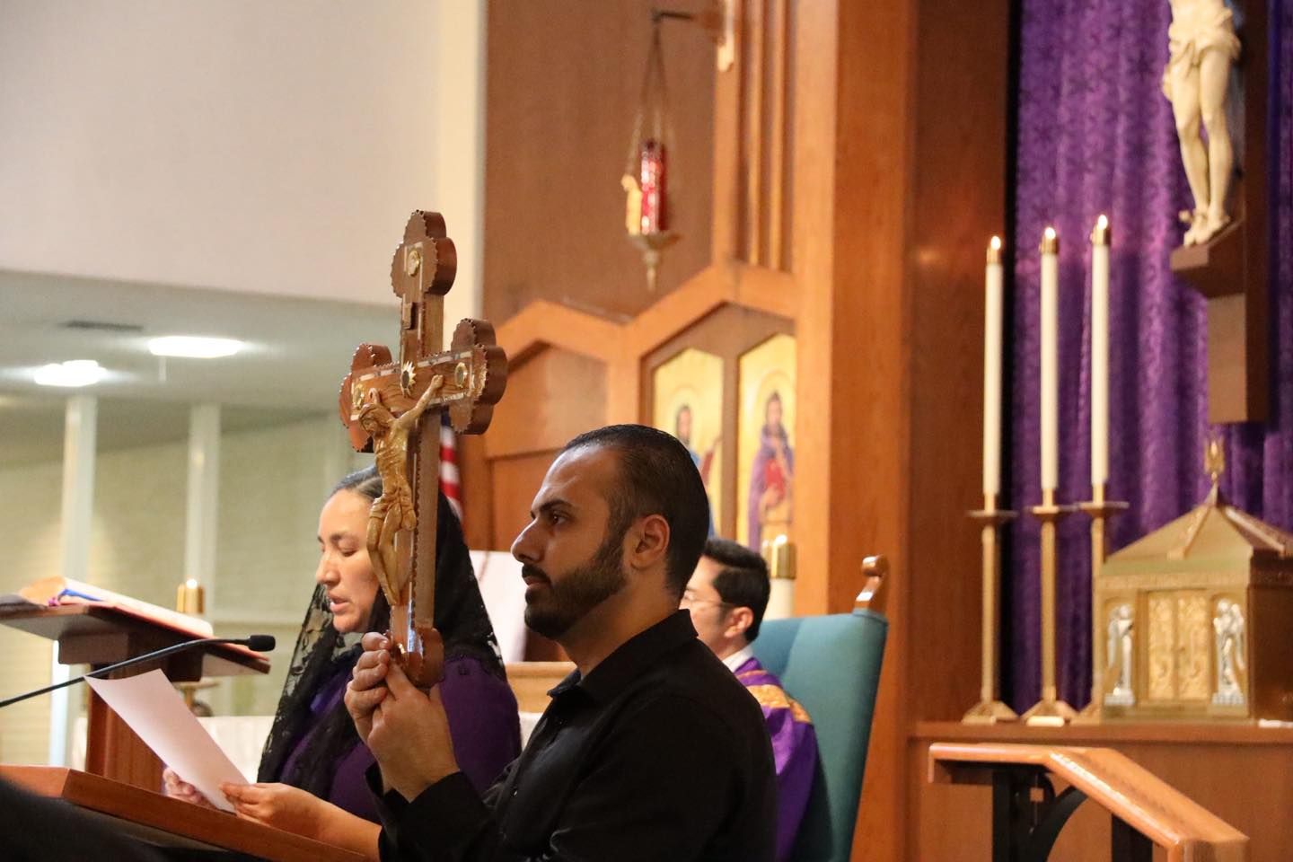 People seated in a church during a service, with a cross and purple altar cloth in the background.