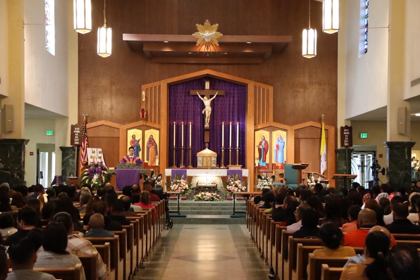 Church interior with congregation seated in pews facing an altar draped in purple and a crucifix above it