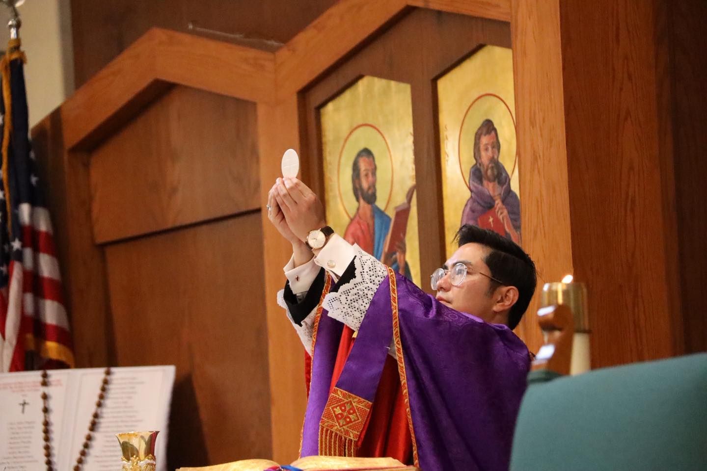 Priest in purple vestments raising a wafer during Mass at the altar