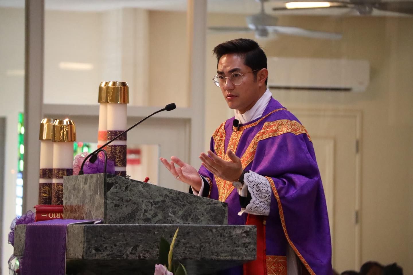 Priest in purple vestments speaking at a church lectern during a service