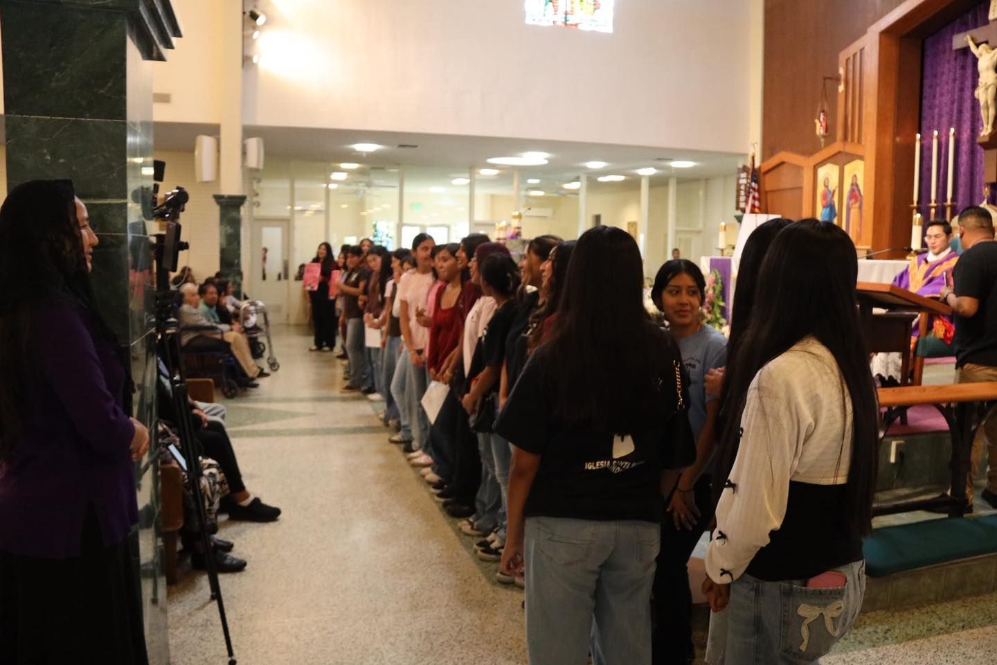 People lined up in a hallway outside a room, waiting near a doorway and reception desk.