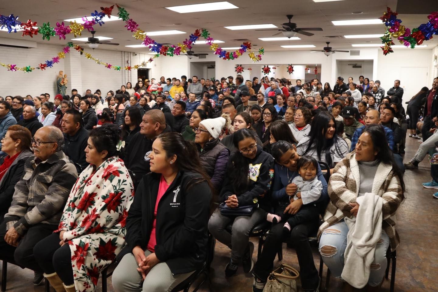 Large crowd seated in a decorated hall, watching an event or presentation.