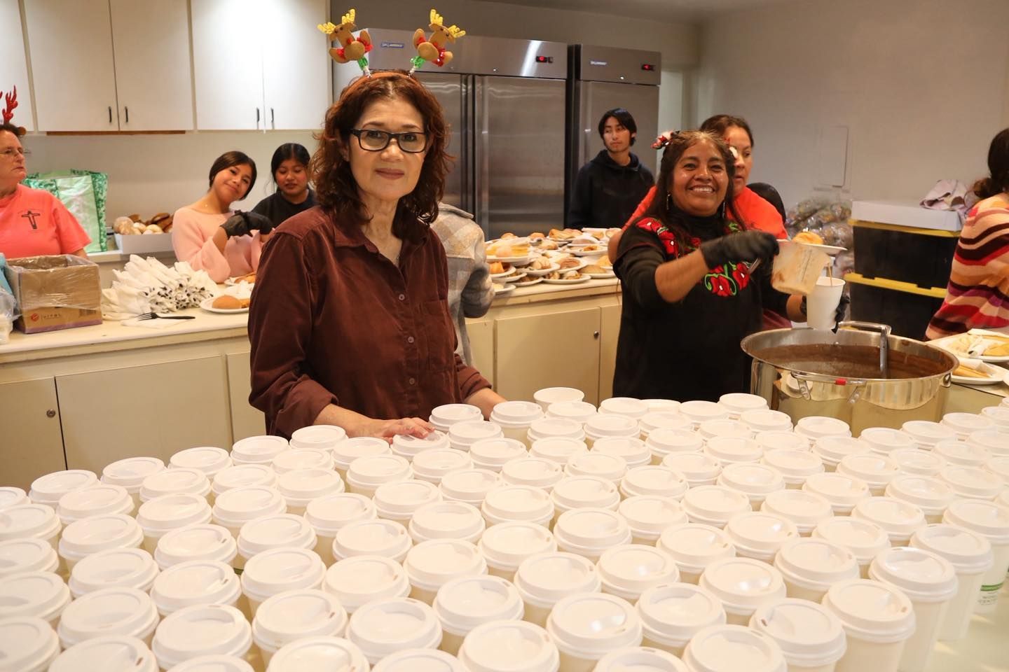 Volunteers behind a table stacked with rows of white cups at an indoor event