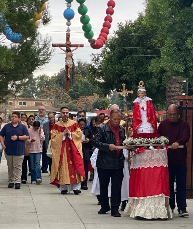 Religious procession with a crucifix, a statue on a decorated float, and people walking outdoors on a street.