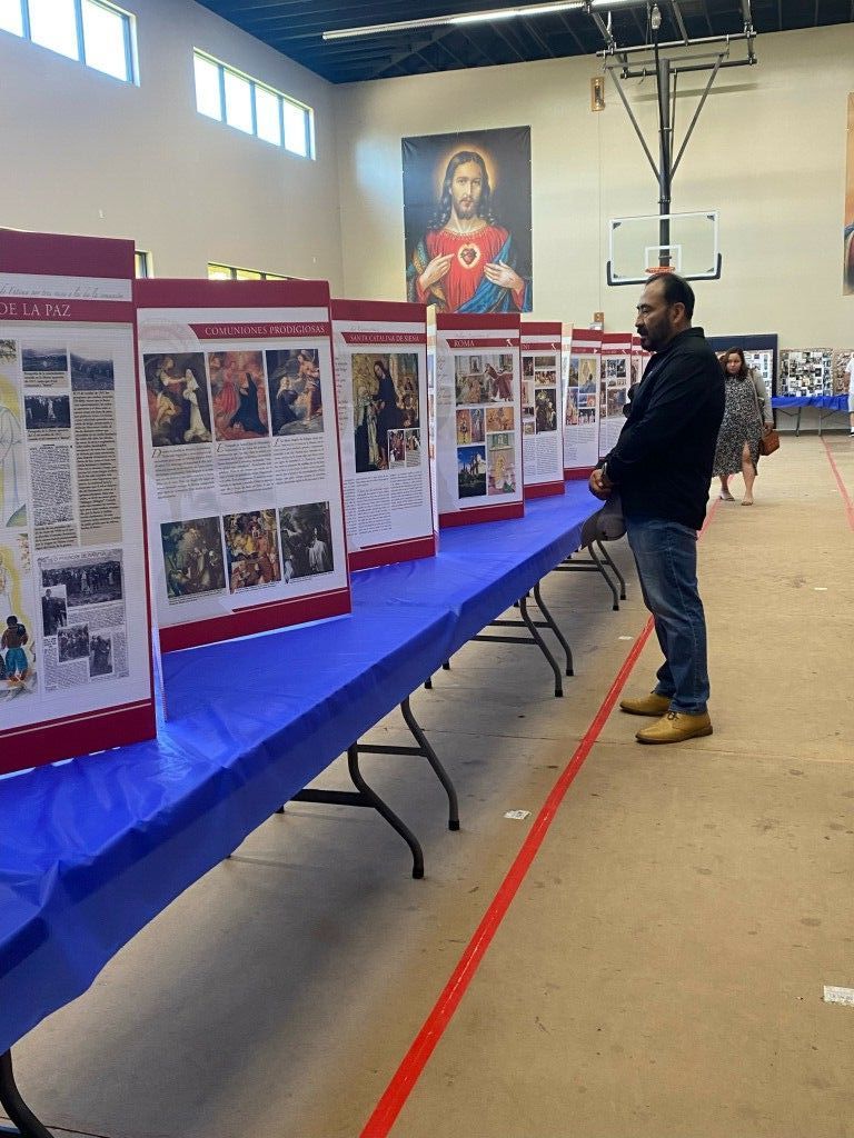 Man standing beside poster boards displayed on a blue tablecloth in a gymnasium or hall