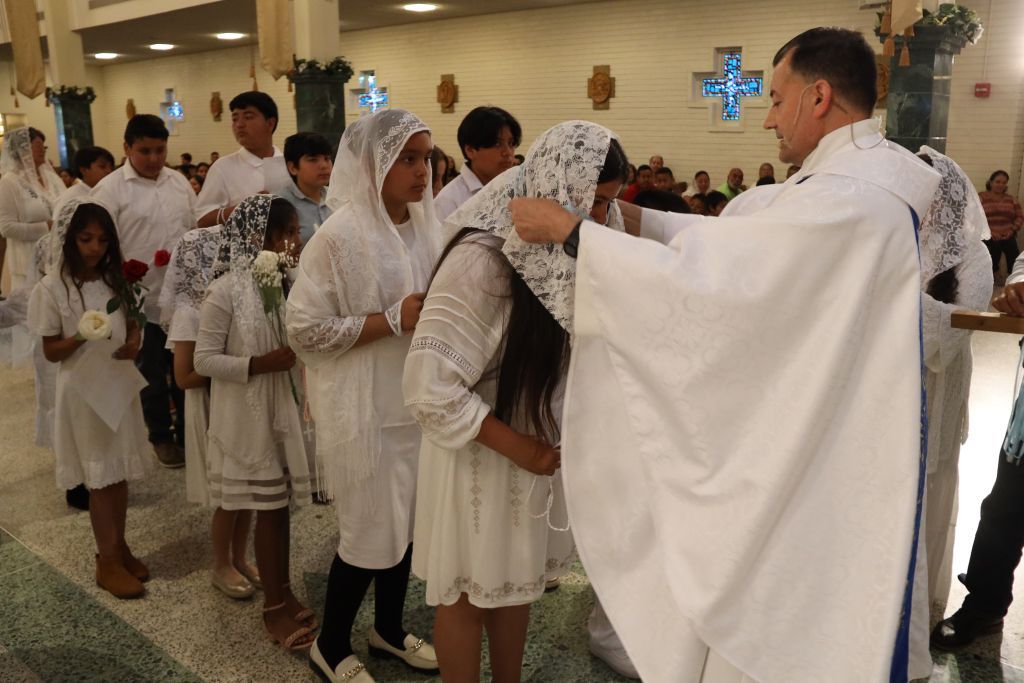 Priest gives communion to worshippers in white robes inside a church