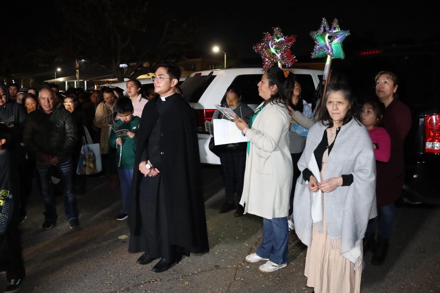 People gathered at night holding star-shaped balloons, with one person in a black cloak at center.