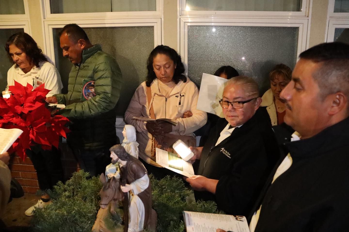 People gathered indoors, holding lit candles and wreaths during a memorial service.