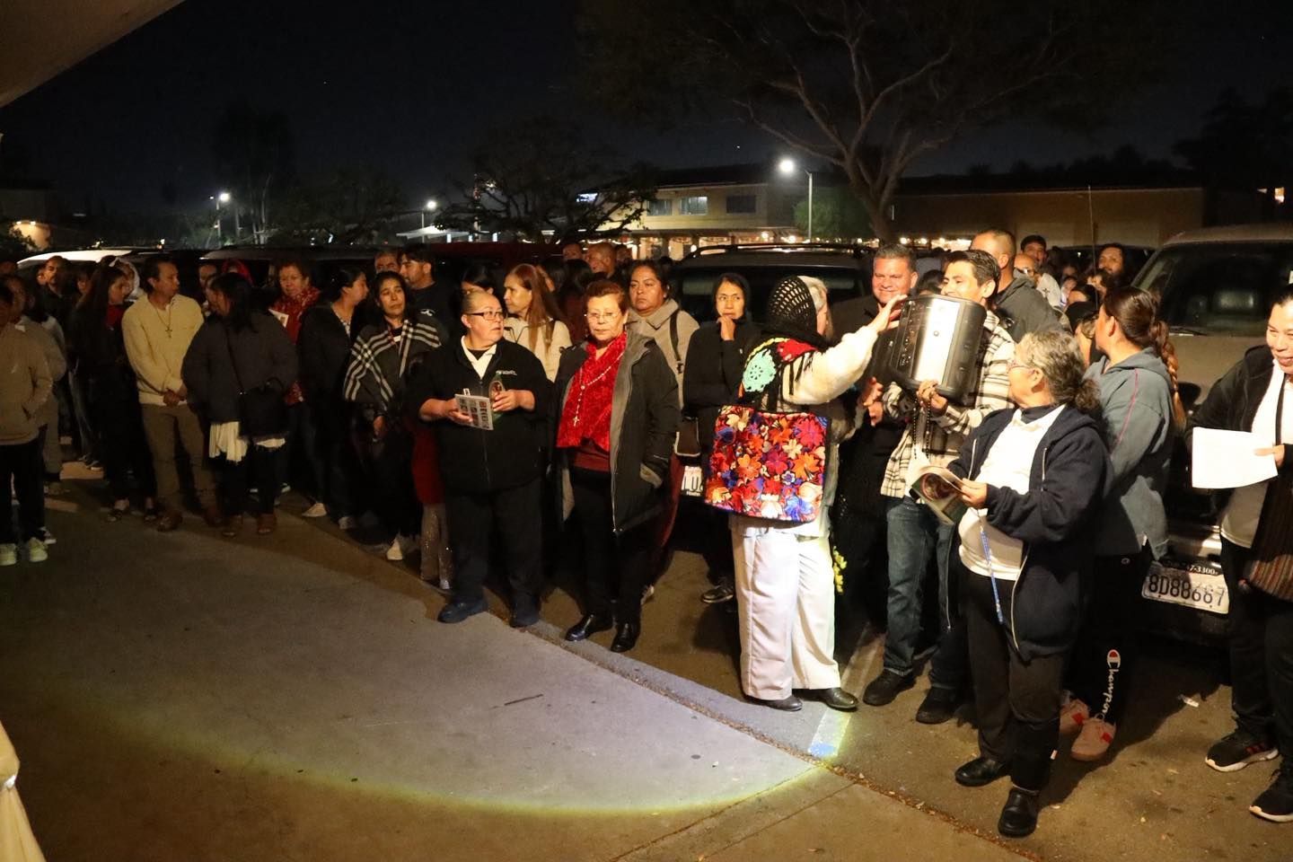 Crowd gathered at night outdoors, holding candles and signs during a vigil or protest