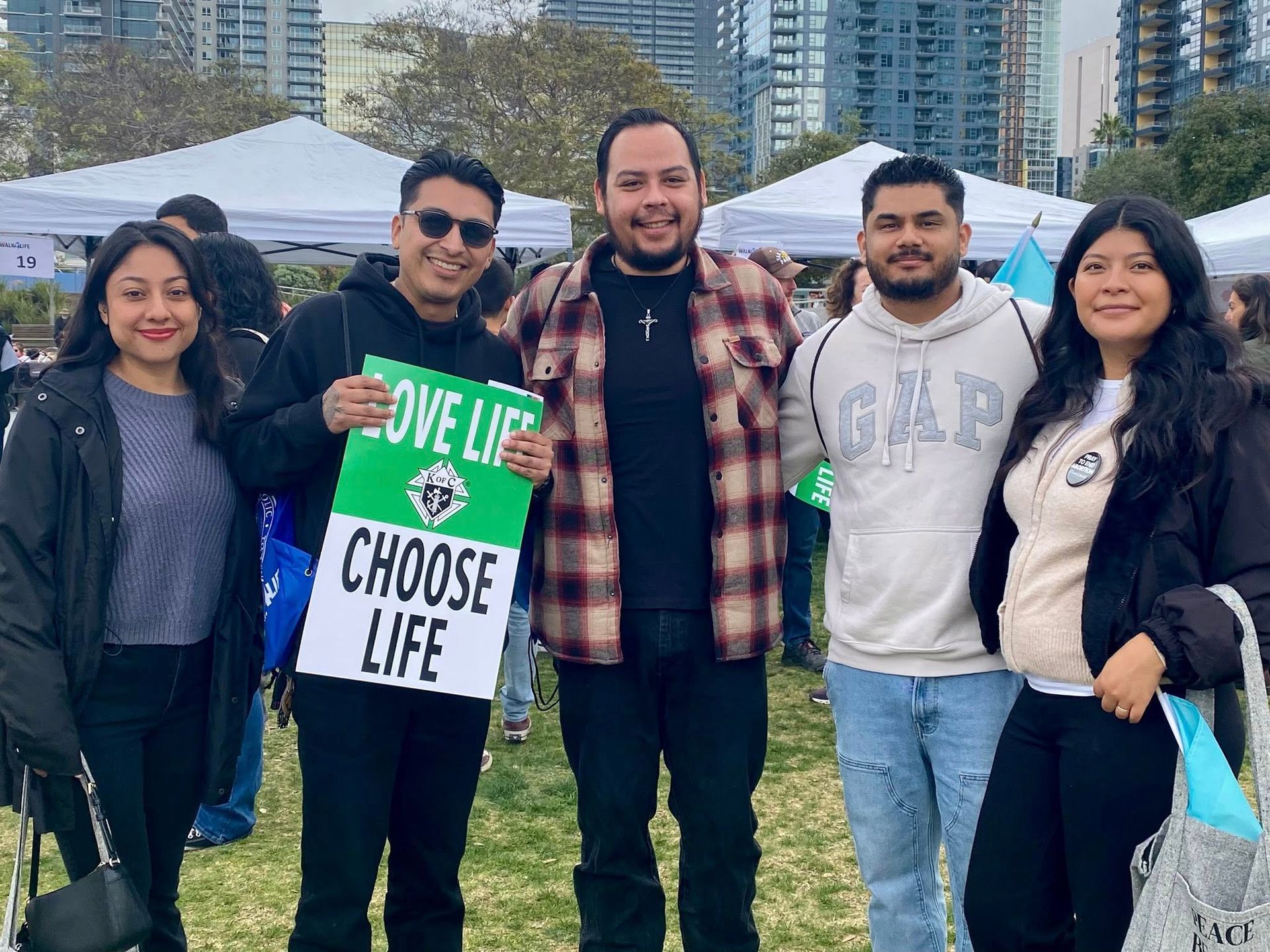 Five people posing outdoors at a park, holding a green and white “Give Life, Choose Life” sign.