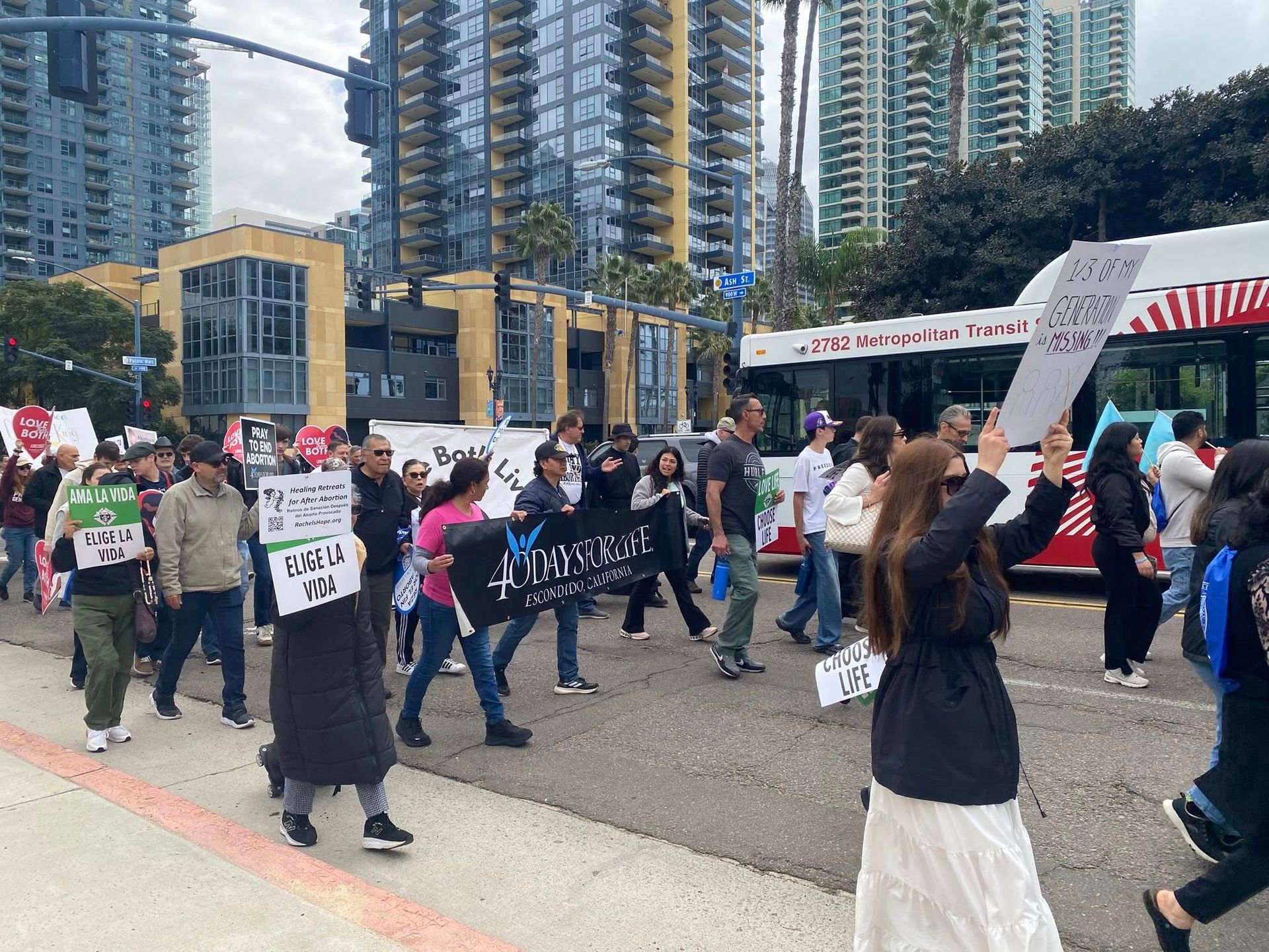 Crowd marches with protest signs on a city street beside tall apartment towers