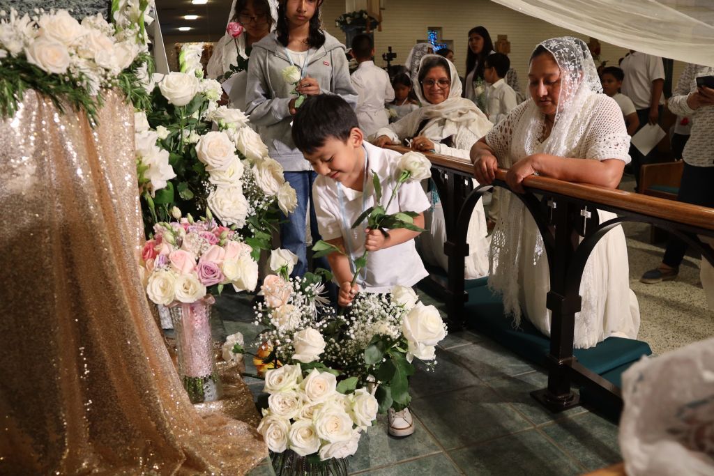 Child leaning over flower-covered fountain at a wedding reception, with guests watching nearby