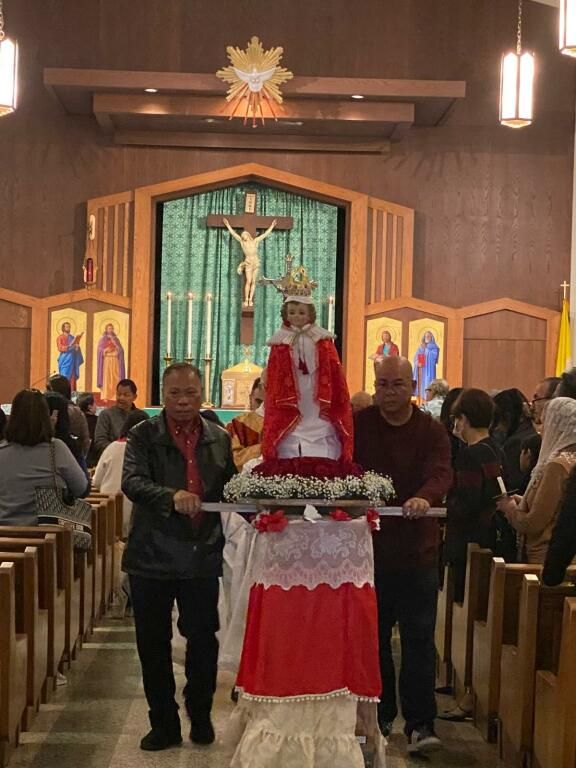 Church procession with statue of a saint in a red robe carried down the aisle
