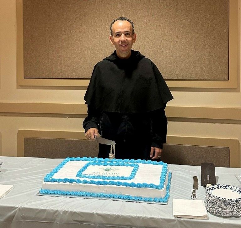 Person standing behind a blue-and-white frosted cake on a table in a banquet room