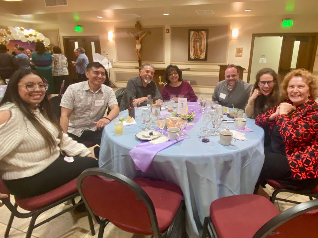 Group of people seated around a banquet table in a warmly lit dining room, smiling and posing together.