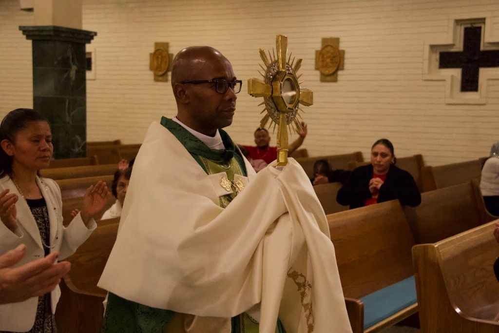 Priest in white robes carrying a gold monstrance in a church during a procession
