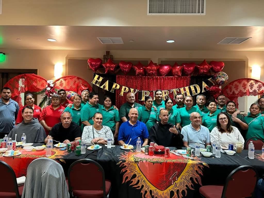 Large group posing at a festive banquet with red balloons and a “Happy” banner