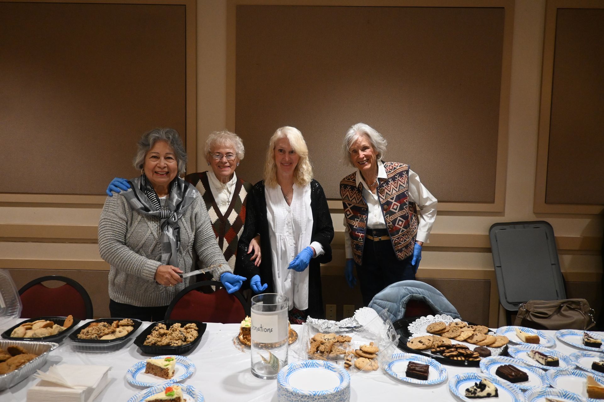 Four people standing behind a dessert table with trays of pastries and a cake in a banquet room