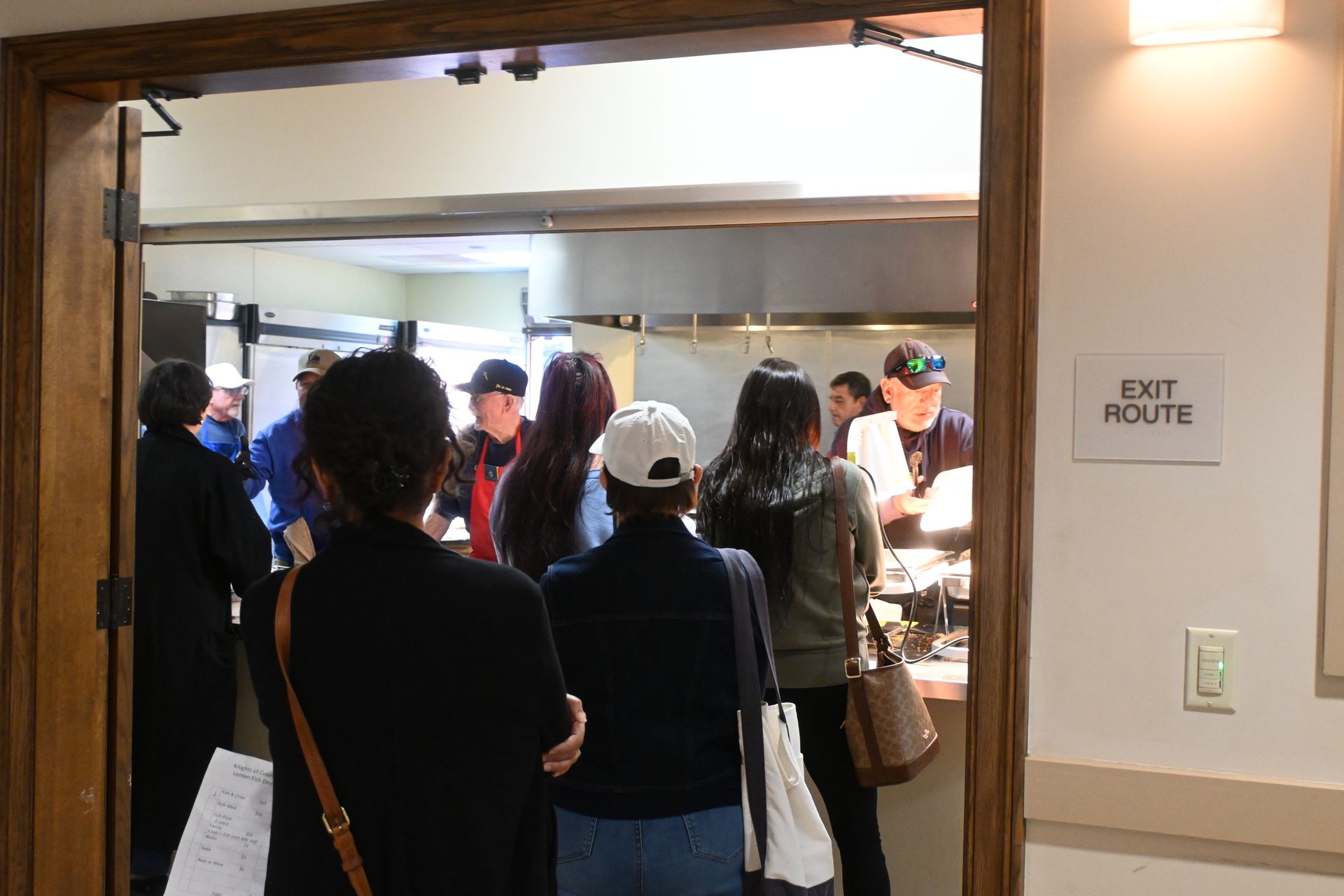 People gathered at a doorway in a hallway, with an EXIT ROUTE sign on the wall.