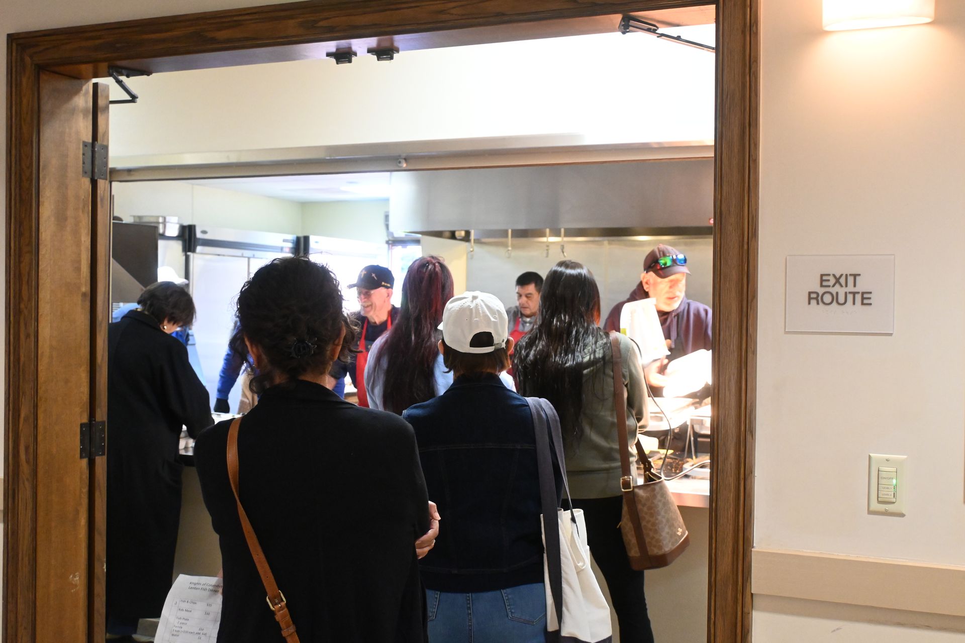 People gathered in a doorway at an event, with an “EXIT ROUTE” sign on the wall.