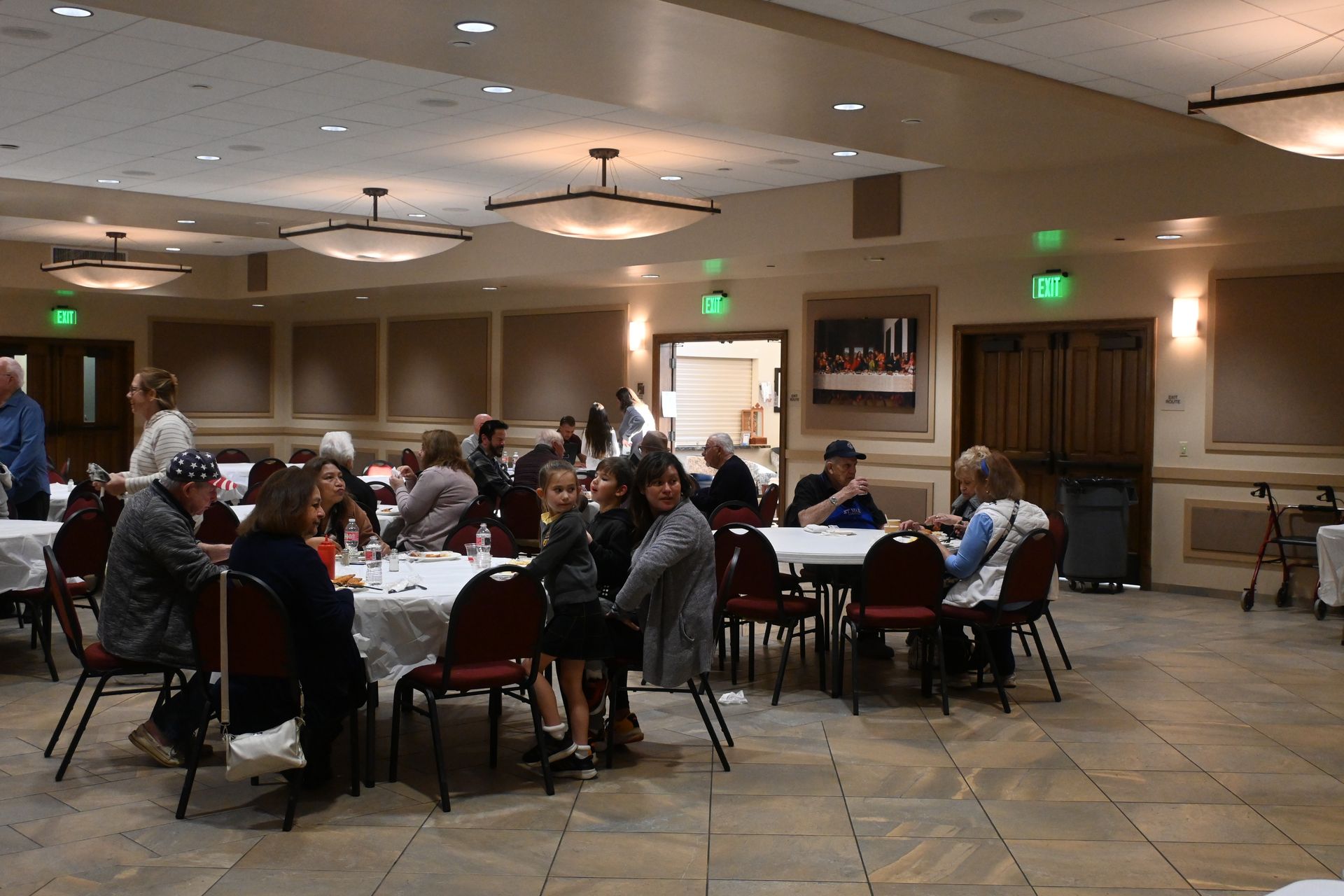 People seated at round tables in a banquet hall with warm lighting and green exit signs.