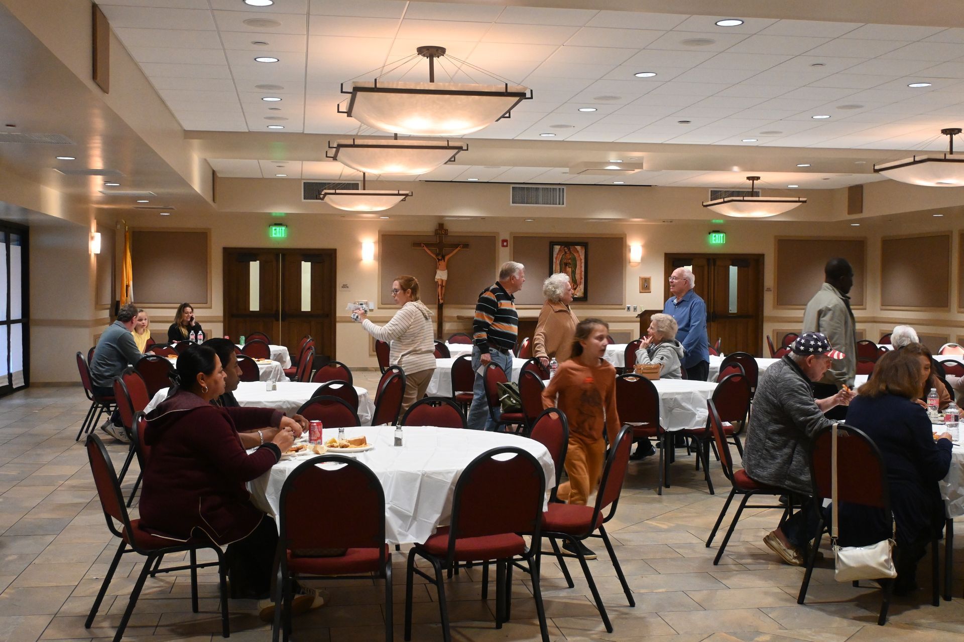 People seated at round tables in a community hall, talking during a social gathering.