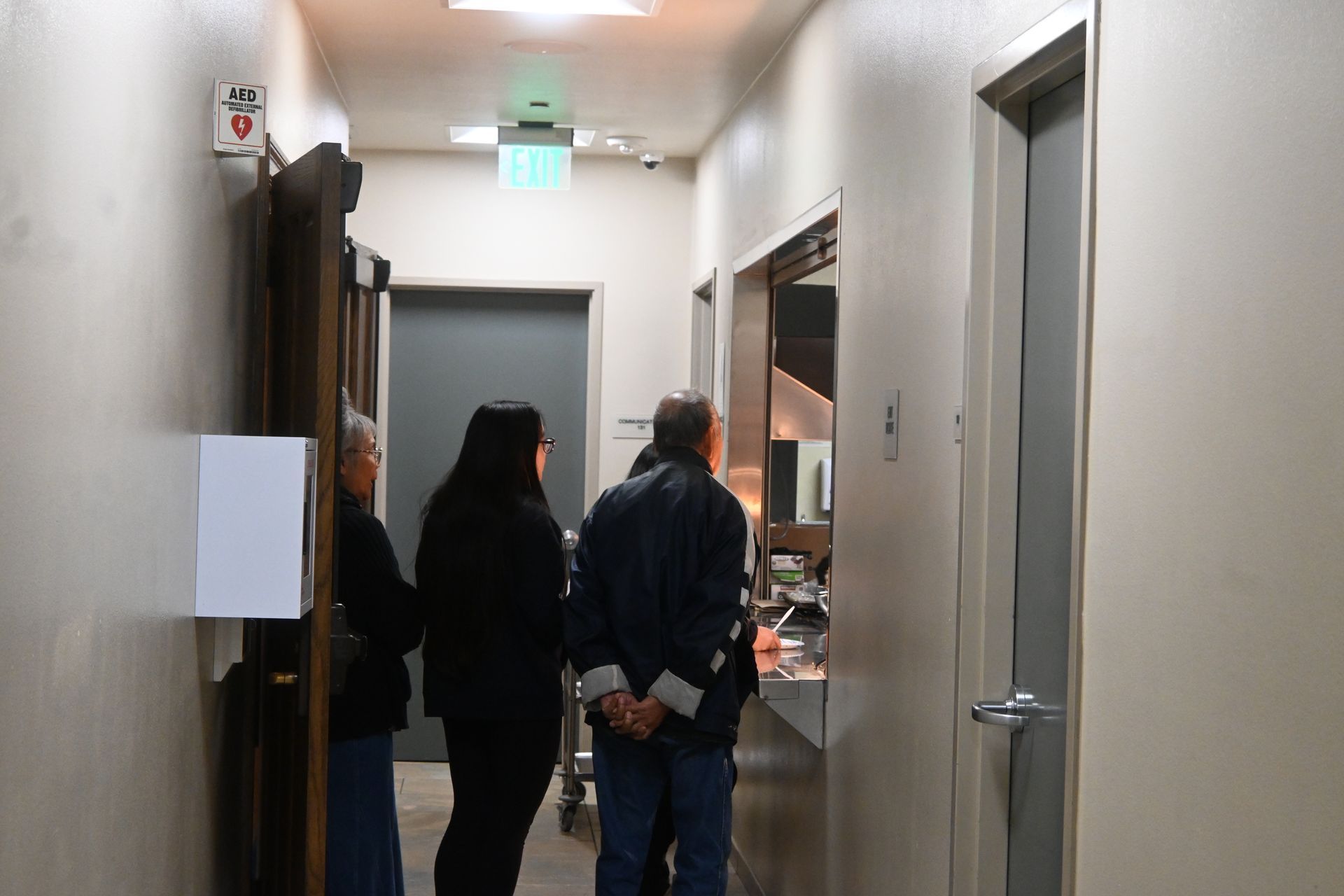 Three people walking down a narrow hallway in an office or apartment building