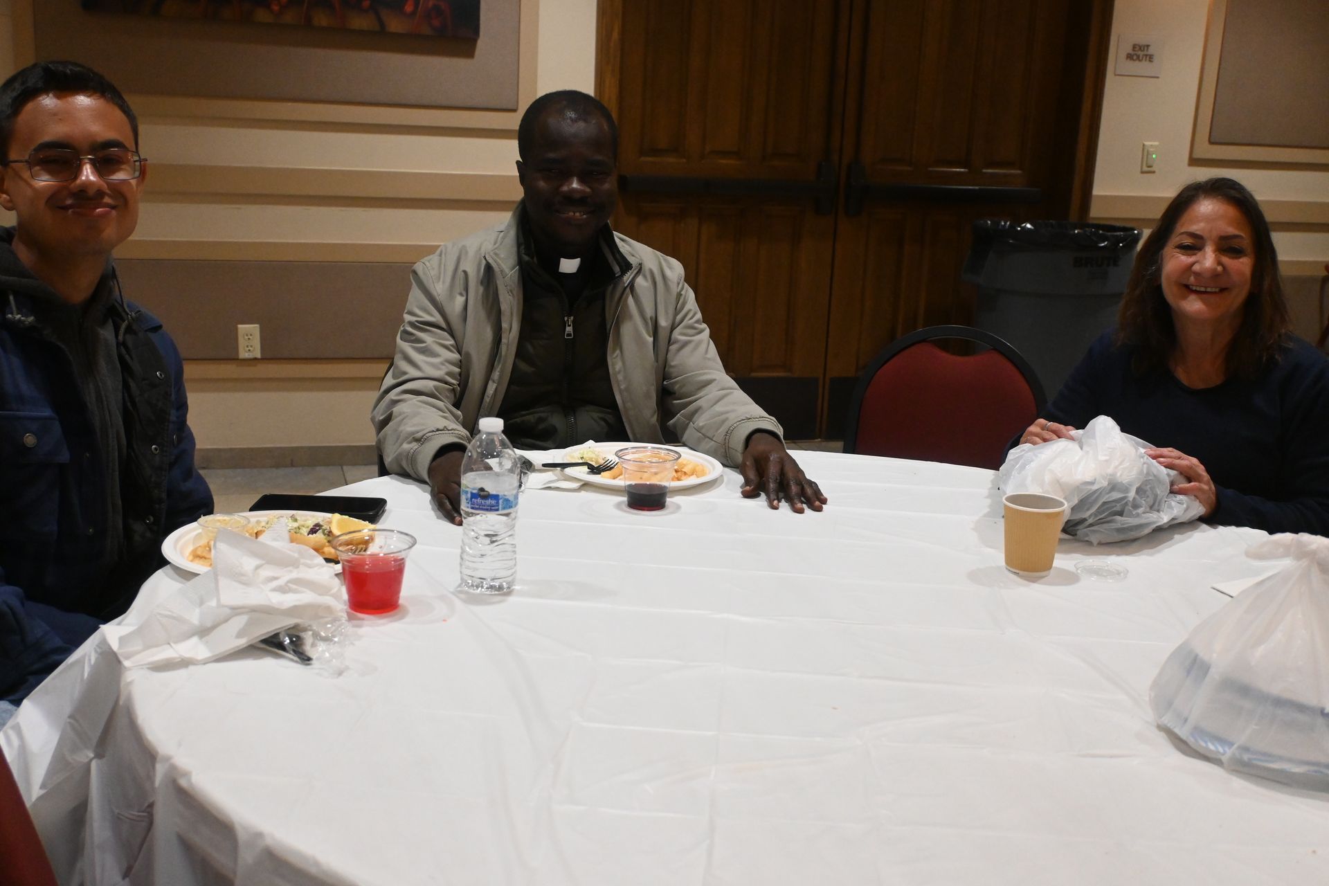 Three people seated at a banquet table with drinks and food in a conference room