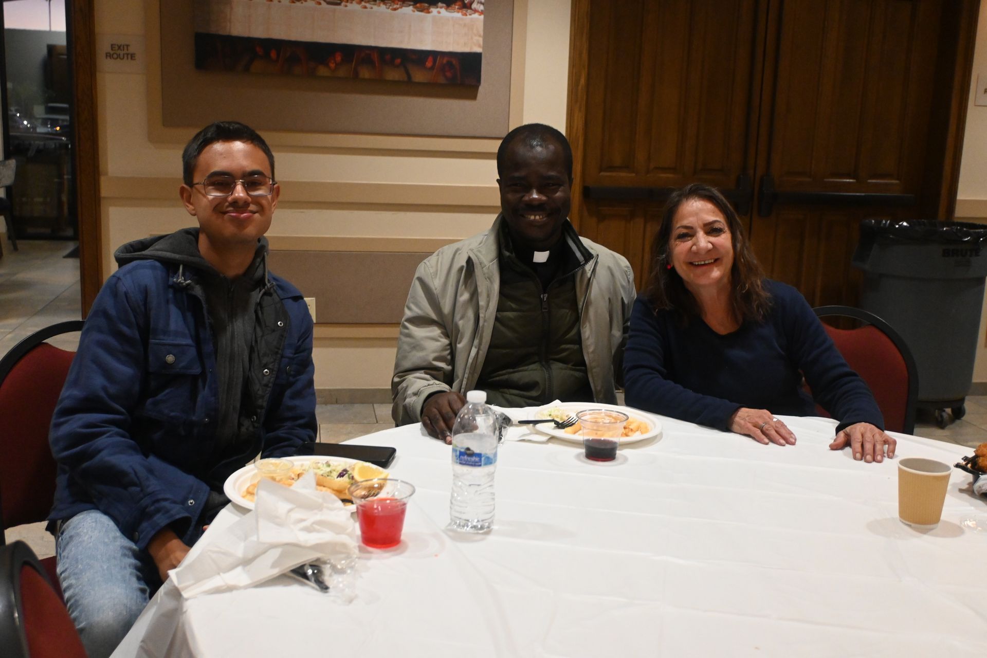 Three people seated at a table indoors, smiling at the camera with drinks and plates in front of them.