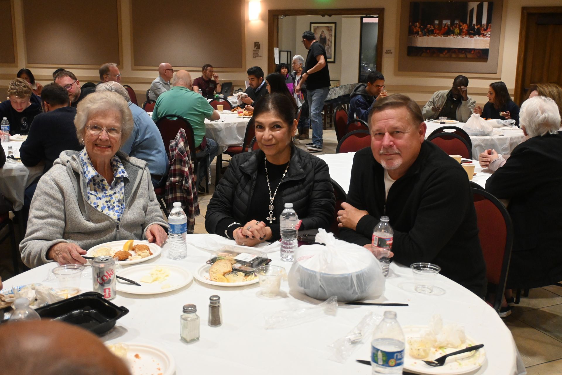 People seated at a banquet table in a dining hall, smiling and eating during a group event.