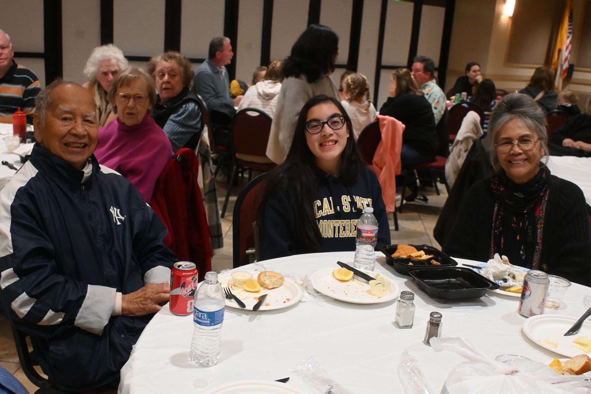 People seated at banquet tables in a dining hall, smiling and chatting during a meal