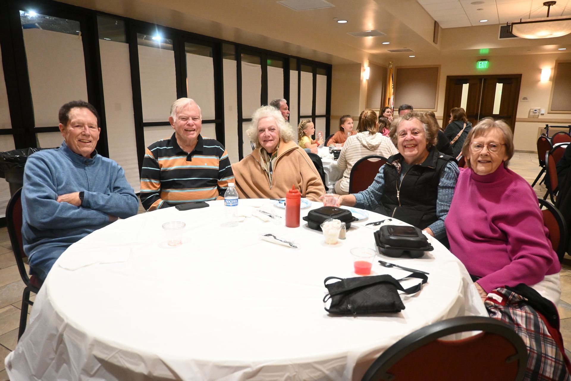 Five people seated at a round table in a warmly lit dining room, smiling at the camera.