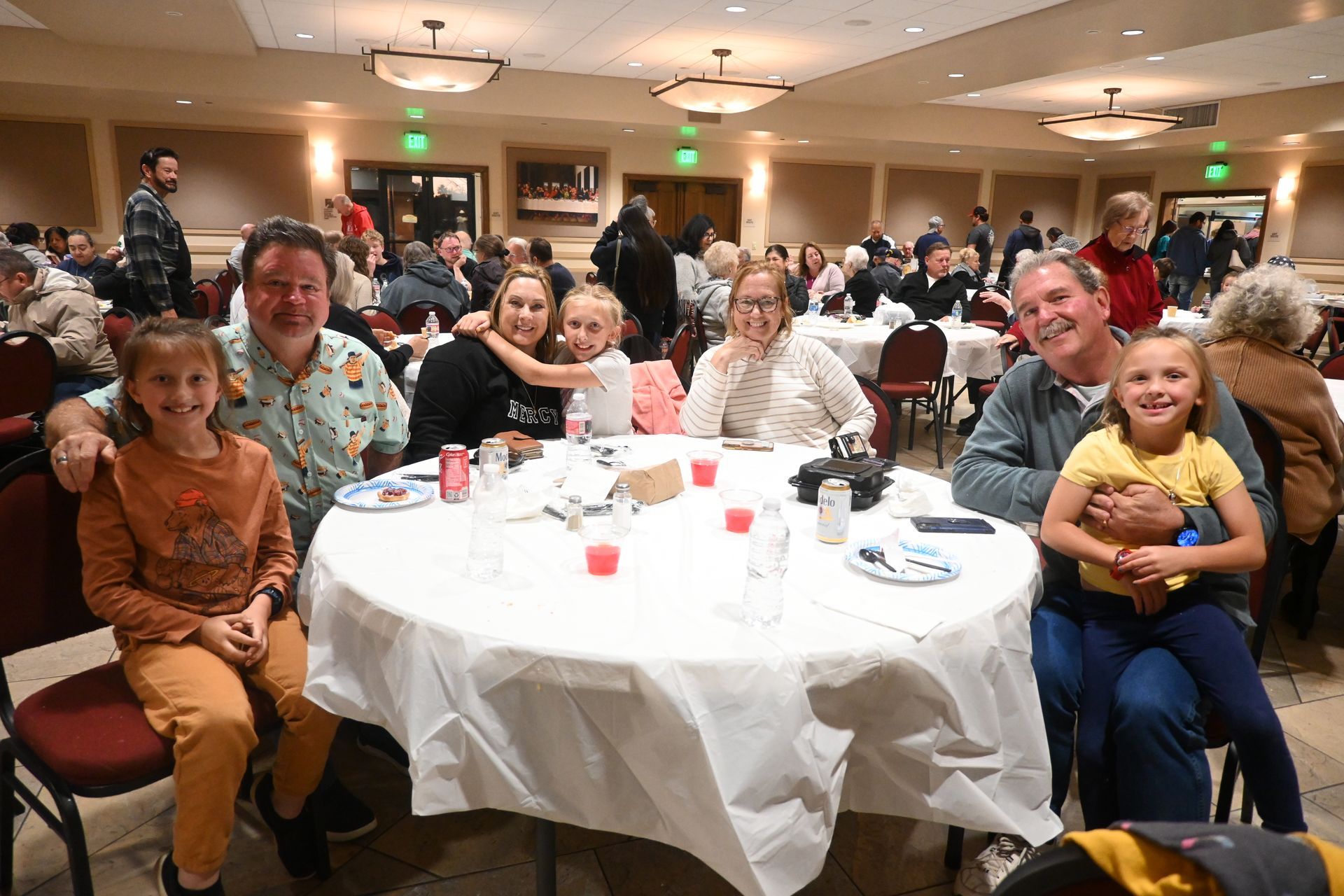 People seated at a banquet table in a crowded dining hall, smiling and posing for a photo.