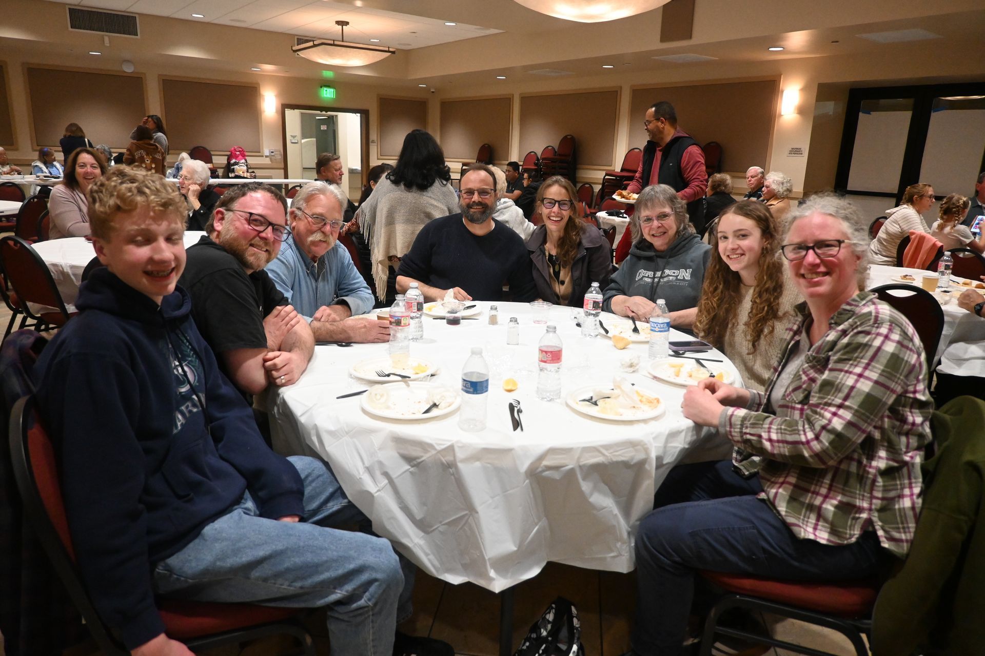 Group of people seated around a banquet table at a banquet hall, smiling and chatting during a meal.