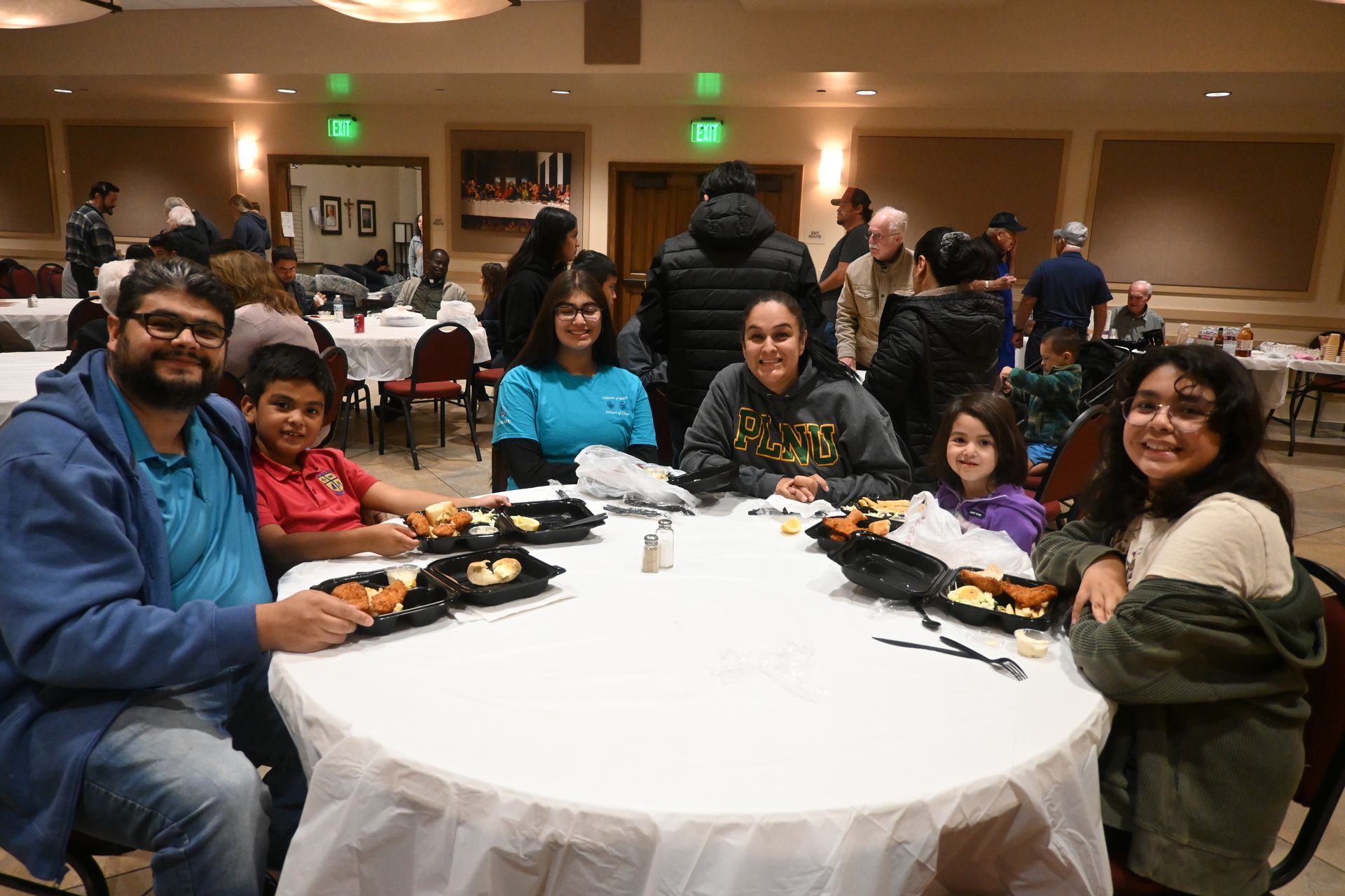 Group seated around a round banquet table in a warmly lit dining hall, smiling at the camera.