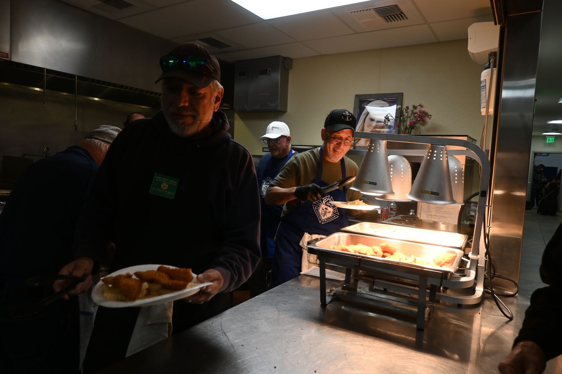People serving food from a buffet line in a dim dining room