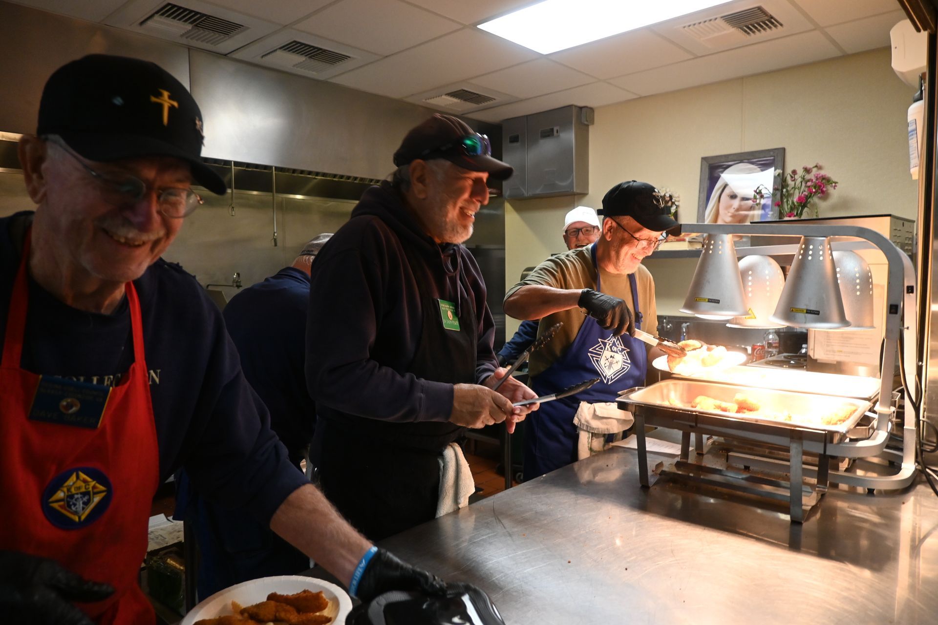 Volunteers serving food at a buffet counter under heat lamps