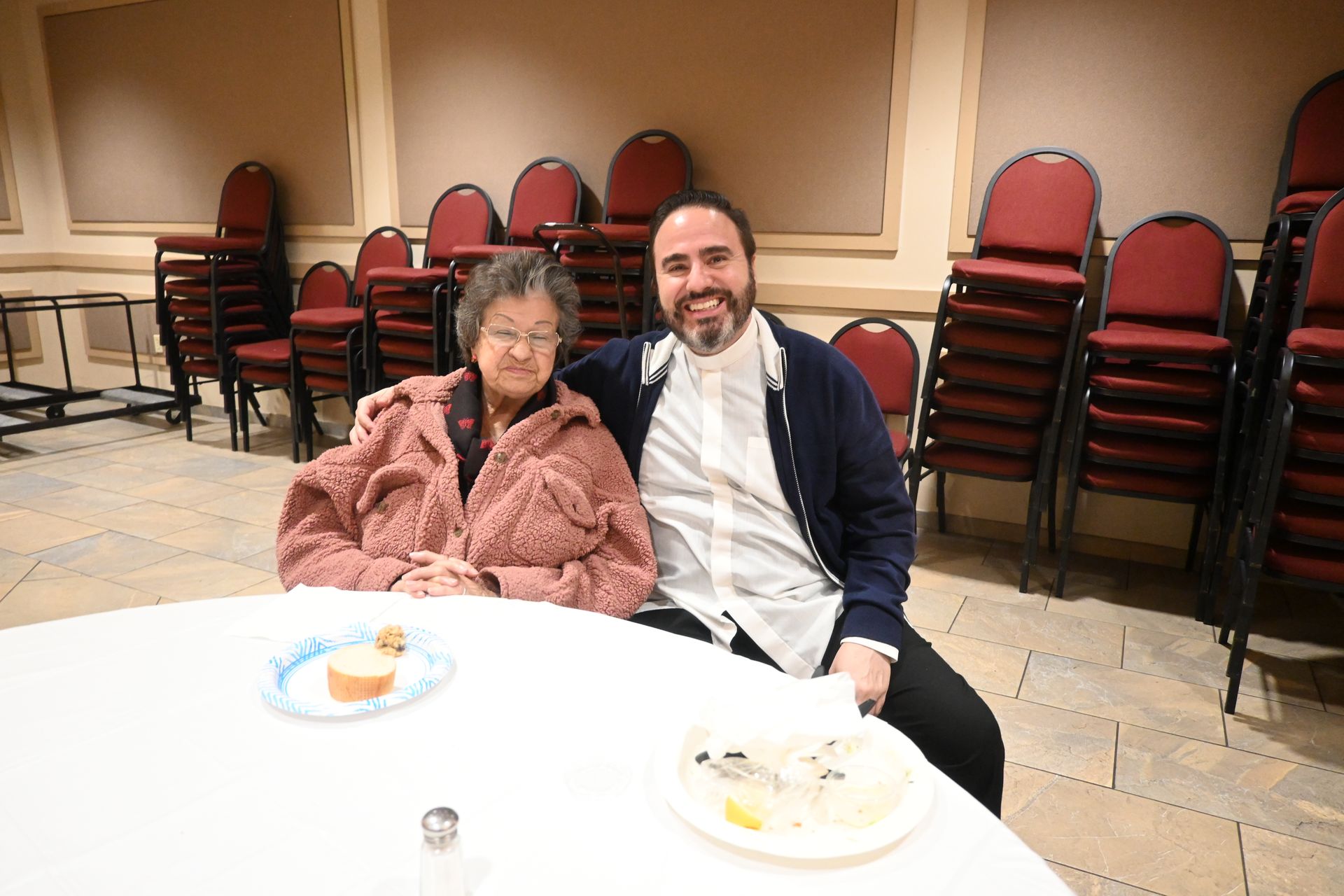 Two people seated at a round table in a banquet hall, smiling with plates in front of them.