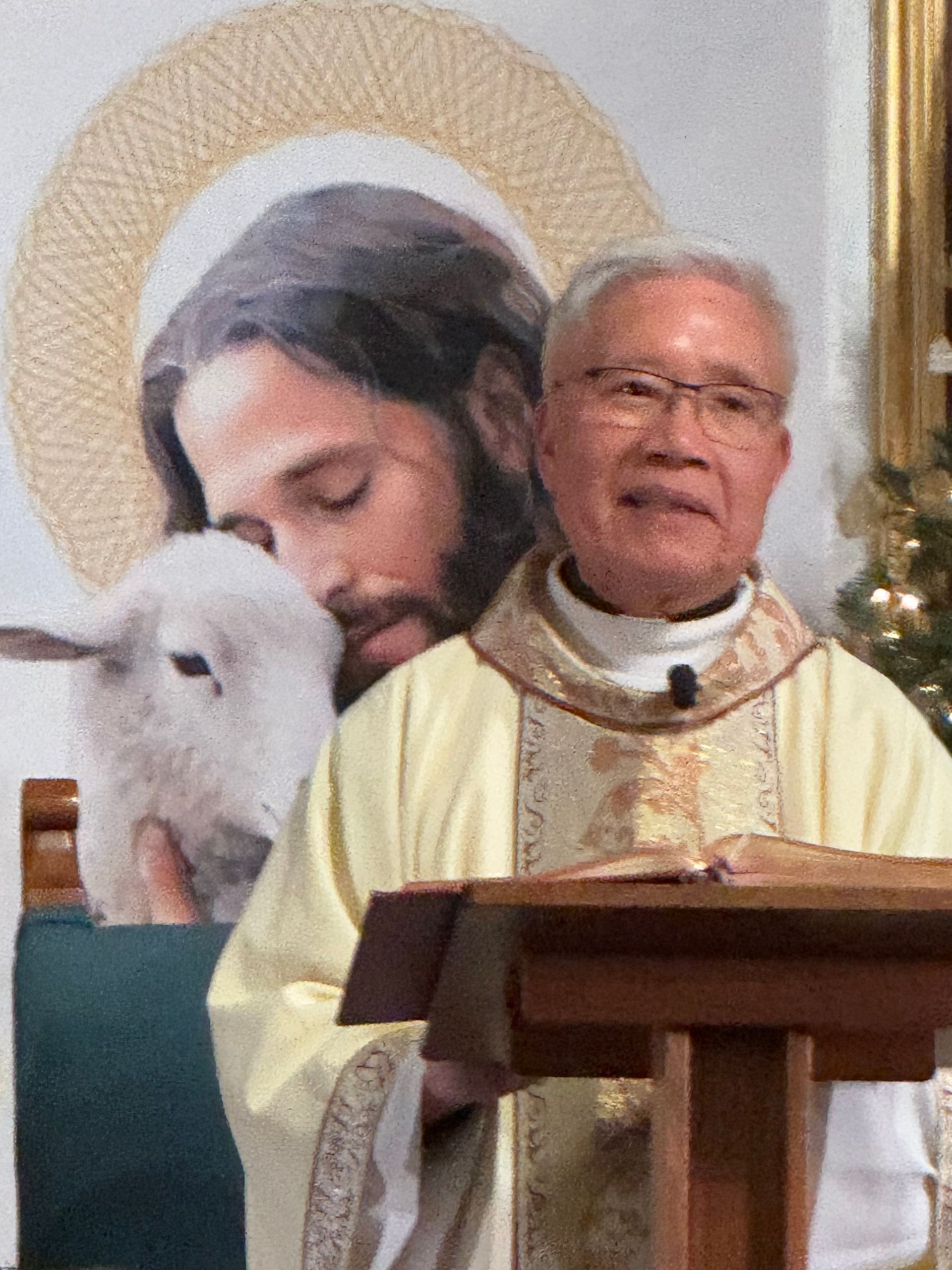 Priest at a lectern in white and gold vestments, with a Jesus-and-lamb mural behind him.