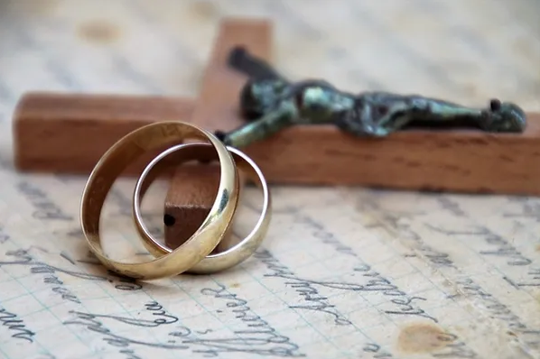 Two gold wedding bands beside a crucifix on a handwritten letter.