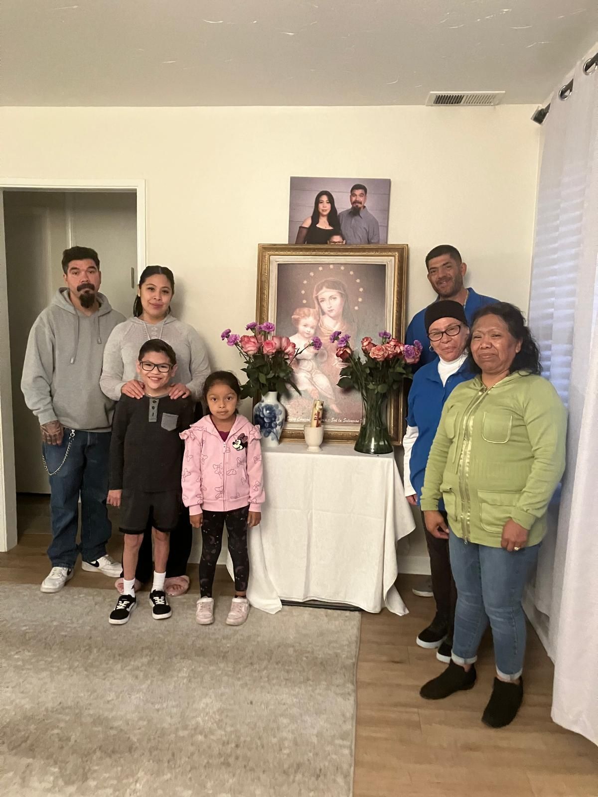 Family gathered indoors around a memorial table with flowers and framed photos