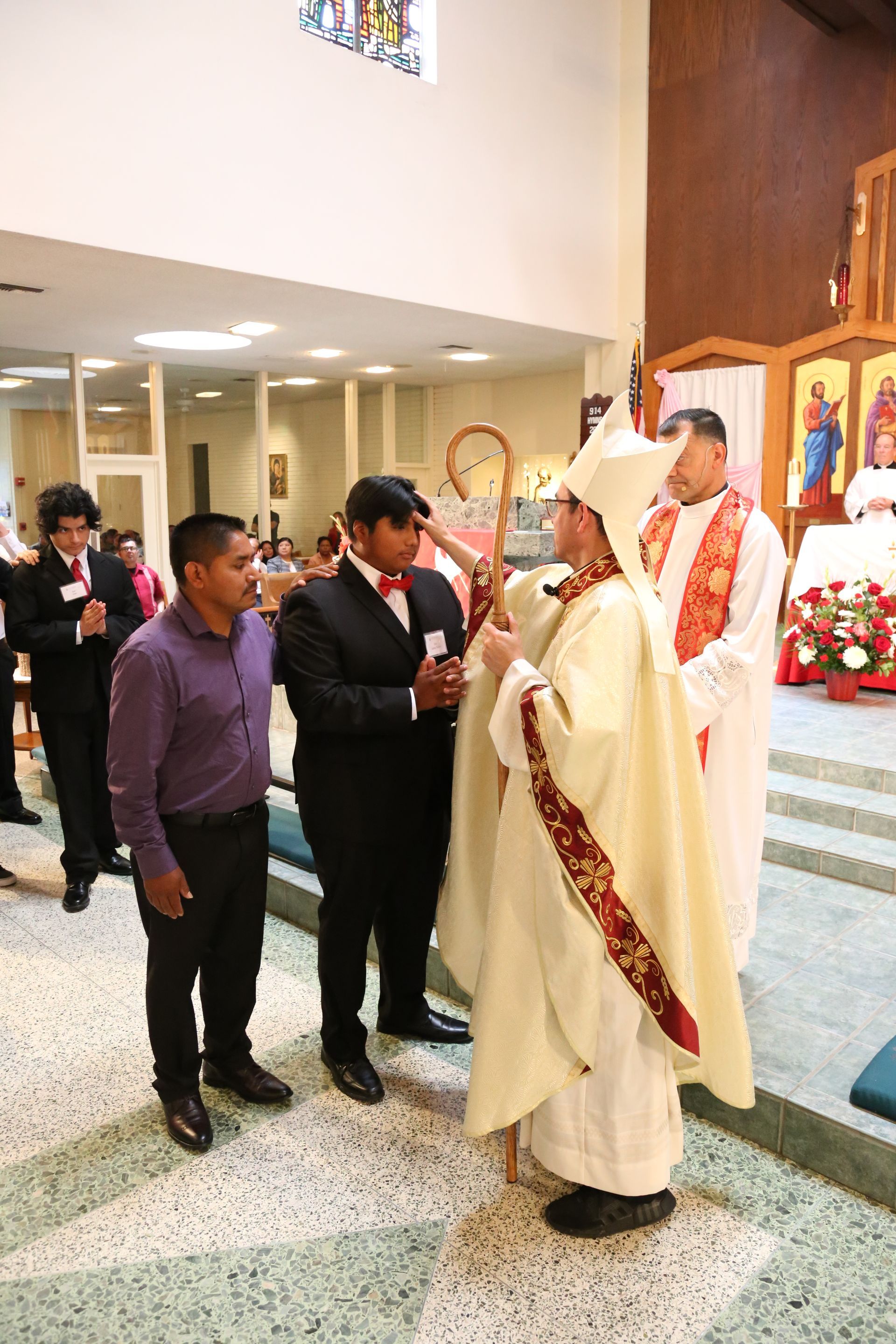 Priest in white vestments greets people inside a church during a service