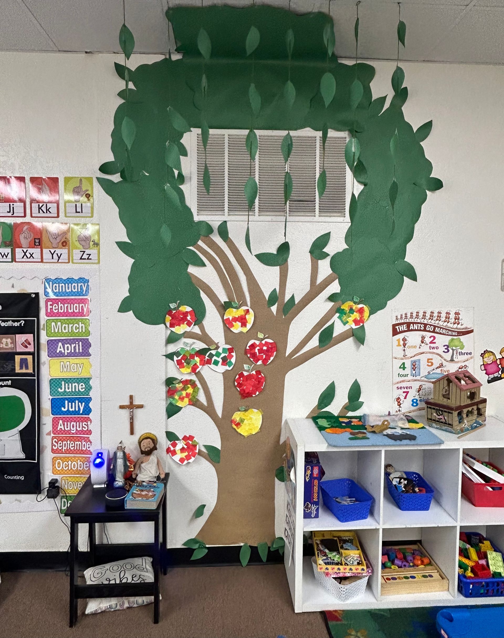 Classroom bulletin board shaped like a tree with children's artwork, bookshelves, and cubbies nearby