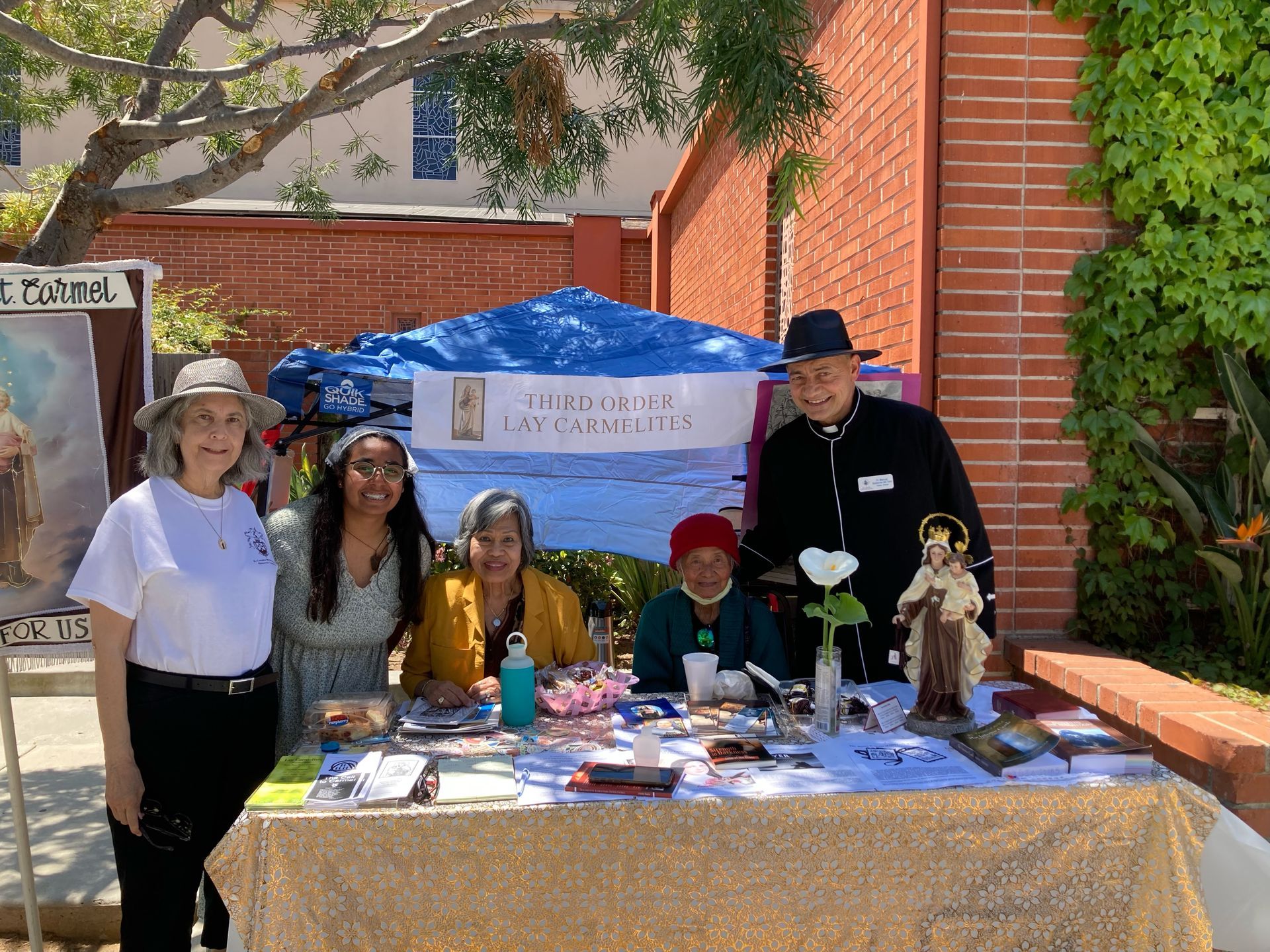 Five people stand behind a table with pamphlets and flowers at an outdoor community booth.