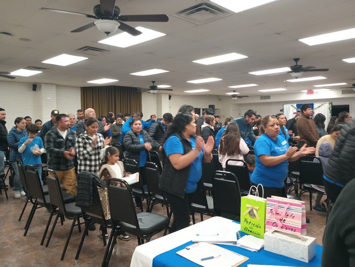 People gathered in a room, standing and clapping during an indoor event.