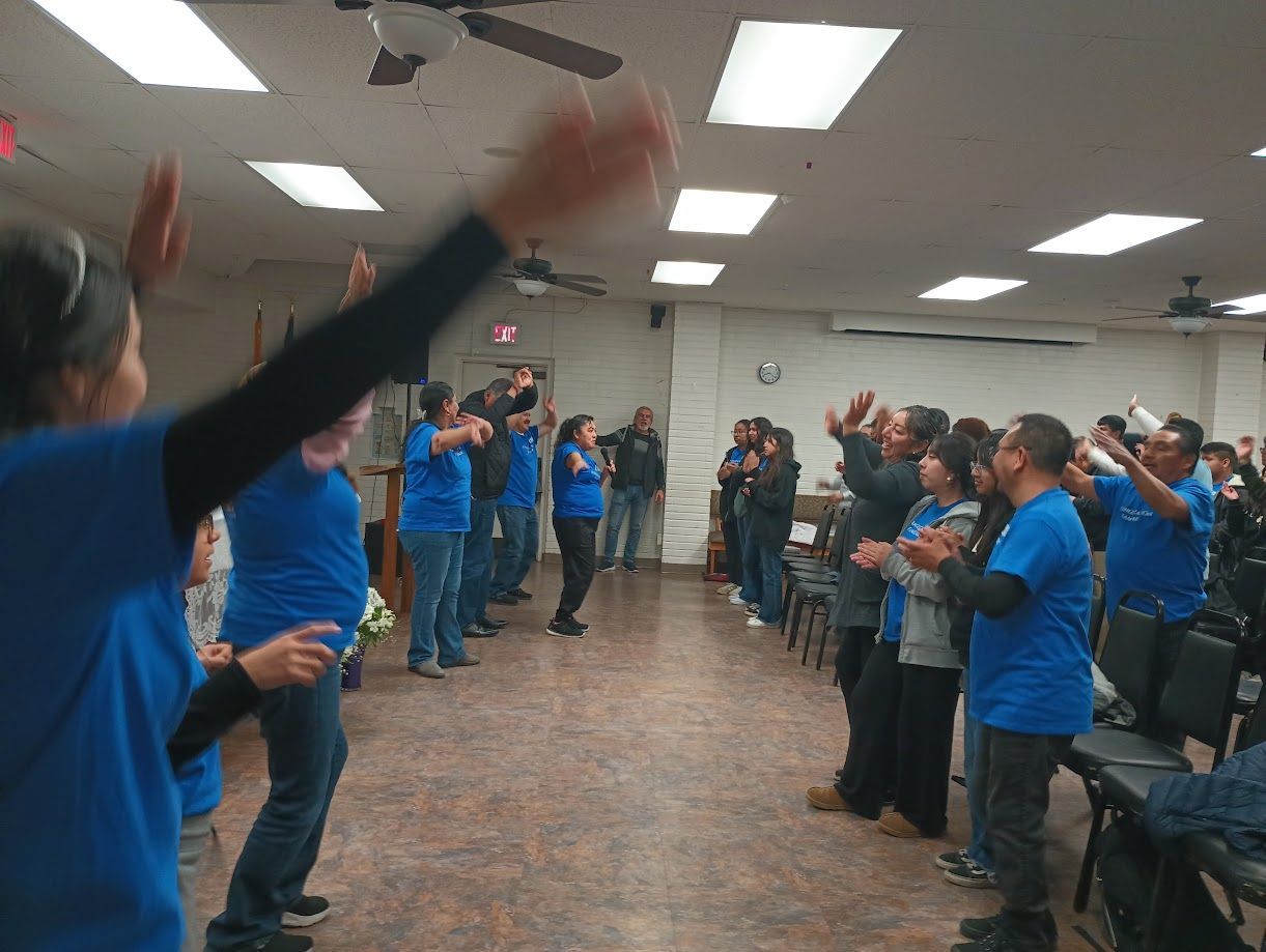 People in blue shirts standing and clapping in a meeting room with a low ceiling.